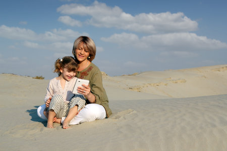 mother and daughter play with tablet in desertの写真素材