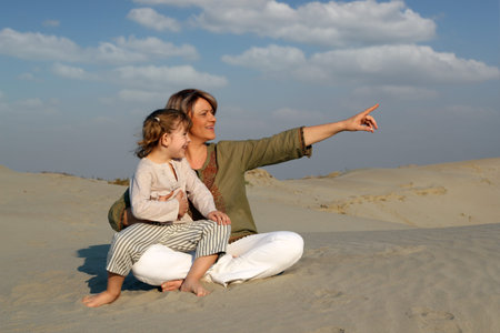 happy mother and daughter sitting on sand family sceneの写真素材