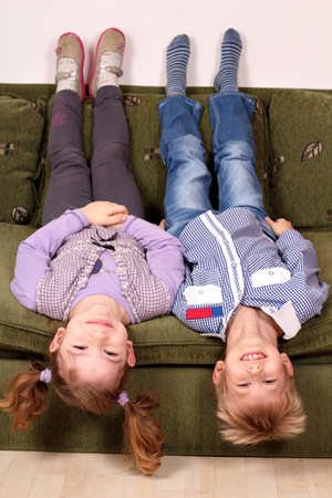 little girl and boy lying upside down on the bedの写真素材