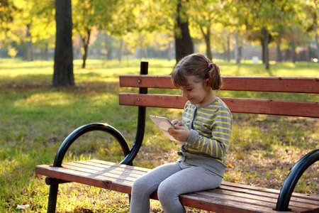little girl play with tablet in autumn parkの写真素材