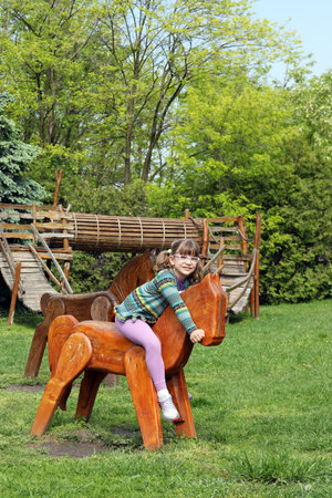 happy little girl riding wooden horse on playgroundの写真素材