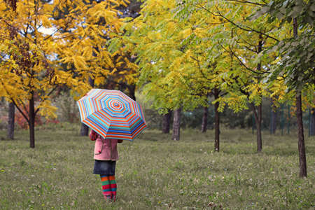 little girl with umbrella in park autumn seasonの写真素材