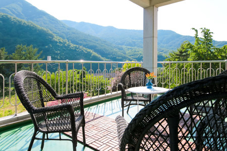 There is the Alps in the back, chairs made of rattan on the terrace, and vases on small tablesの写真素材