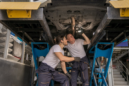 Caucasian car mechanic and automotive team using torch to check a suspension system parts in tire shop. Senior professional vehicle mechanic repair automobile in garage workshop. Auto repair serviceの写真素材