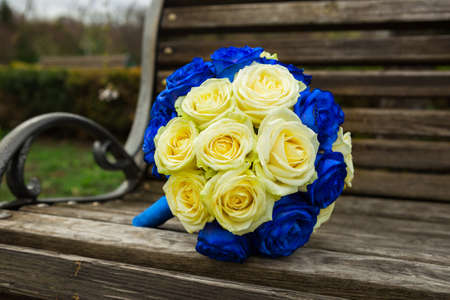 Bright wedding bouquet with cream and blue roses on a wooden bench in the parkの写真素材