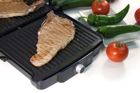 Black electric grill cooking meat with vegetablesの写真素材