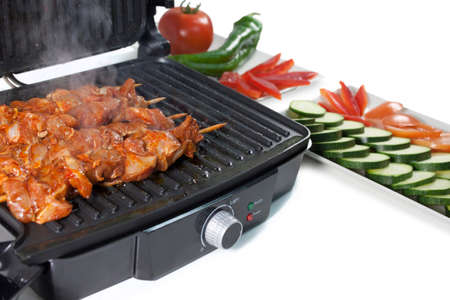 Black electric grill heating meat with vegetablesの写真素材