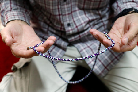 Muslim man praying with prayer beads (Masbahah). Close-up.