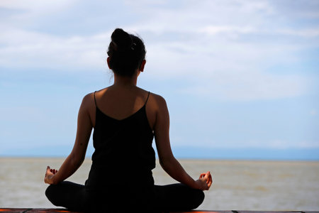 Silhouette of woman meditating in a lotus yoga position in front of the sea. Kep. Cambodia.