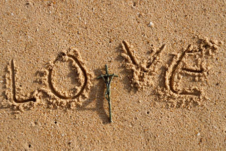 Crucifix and love written in wet sand on beach.の写真素材