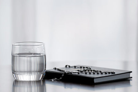 Rosary, glass of water, and holy Bible during Lent. A solemn religious observance that begins on Ash...