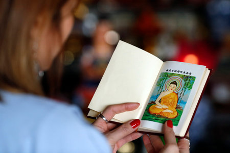 Thien Minh buddhist temple. Woman reading sacred buddhist texts. Shakyamuni Buddha illustration on the first page. France.の写真素材