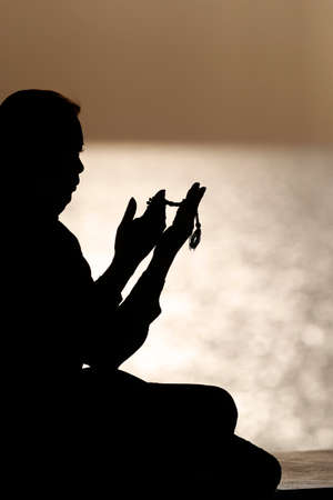 Silhouette of muslim woman holding prayer beads in her hands and praying at sunset. Religion praying concept. United Arab Emiratesの写真素材