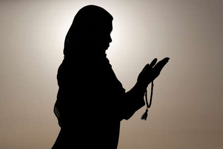 Silhouette of muslim woman holding prayer beads in her hands and praying against the sky. Religion praying concept. United Arab Emiratesの写真素材