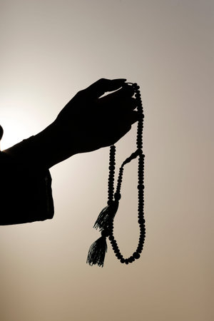 Muslim woman holding prayer beads in her hand and praying against the sky. Religion praying concept....