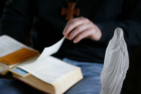 Man reading the Bible. Virgin Mary figurine. France.の写真素材