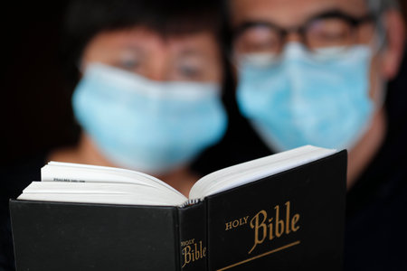 Man and woman reading the bible with a disposable mask to avoid contagious coronavirus (COVID-19). France.のeditorial素材