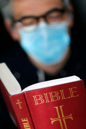 Man reading the bible with a disposable mask to avoid contagious coronavirus (COVID-19). France.