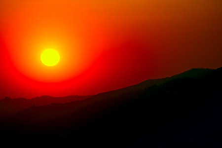 Distant sunset over the silhouettes of the crests of a range of hillsの写真素材