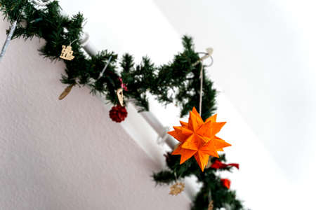 A home made orange origami star is a part of a christmas decoration hanging on the ceiling with some other decoration.の写真素材