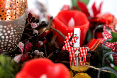 A reindeer clip with a checkered red and white pattern is a part of a christmas wreath together with red candles.の写真素材