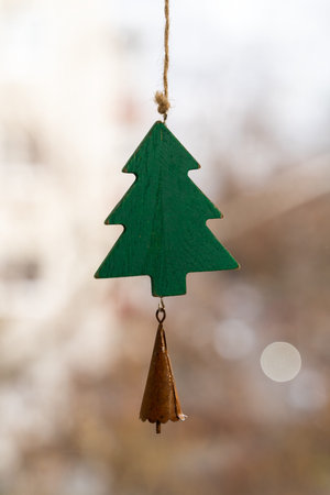 A green wooden christmas tree hangs as a decoration from a brown string and has a small brown bell...