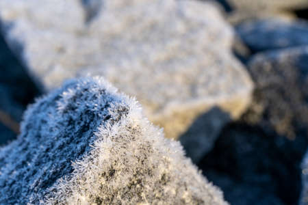 The cold weather on a winter morning generates hoarfrost. It shows up as small ice crystal on a granite block. The background is blurred . Copy space is on the top left.の写真素材