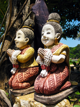 Two colored statues of kneeling praying women in Thailandの写真素材