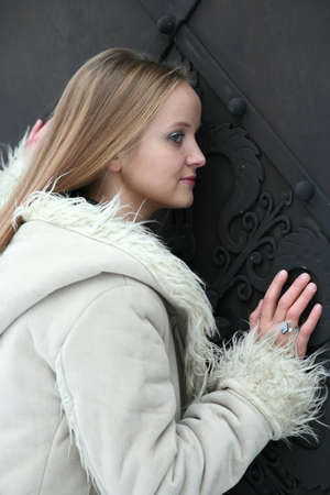 Blond girl in fur coat opening black metal doorの写真素材