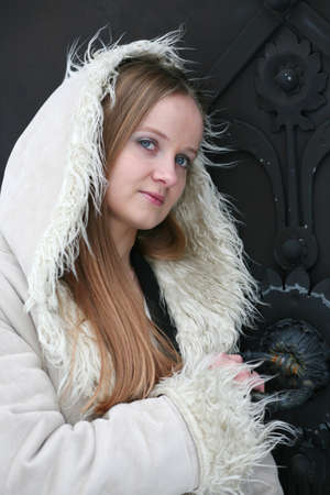 Blond girl in fur coat in front of black metal doorの写真素材