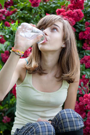 Teenage girl drinking water from the bottle in the flower gardenの写真素材