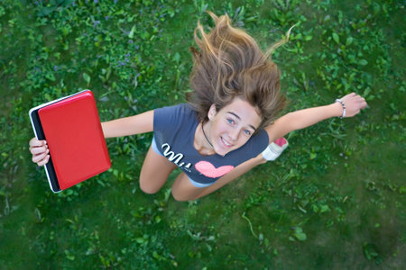 Teenage girl with red laptop jumping up from joyの写真素材