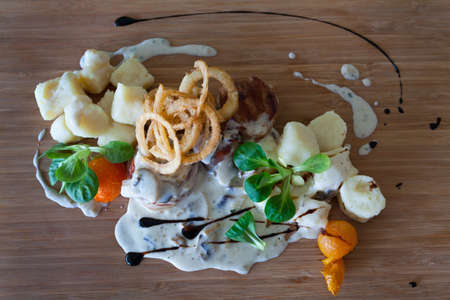Veal medallions wrapped in bacon in a mushroom sauce with gnocchi and onion ringsの写真素材