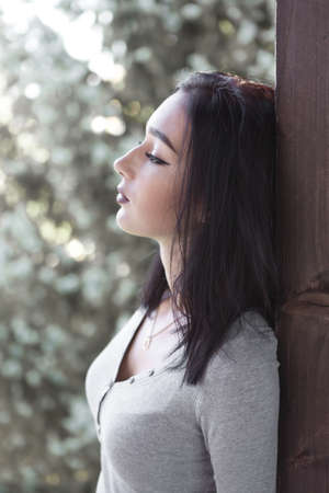 Young woman leaning on a wooden wall, seems sad or depressedの写真素材