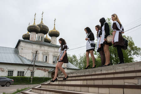 Ustyuzhna Vologda region, Russia - May 22, 2015: schoolgirl in uniform climb the stairs on the background of white stone five-domed Orthodox churchのeditorial素材