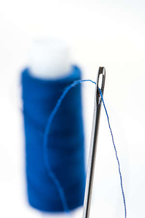 A needle with a wide eye with threaded into it threads. In the background to blur spool of thread.の写真素材