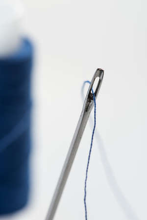 A needle with a wide eye with threaded into it threads. In the background to blur spool of thread.の写真素材