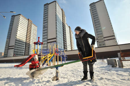 Leningrad, Russia - March 2, 2016: Children's Playground in the new residential area "Devyatkino". A woman with a baby in a swing in a winter sunny day.のeditorial素材