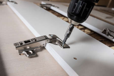 screwing the furniture hinge leaf to the white cabinet in the small wholesale furniture companyの写真素材
