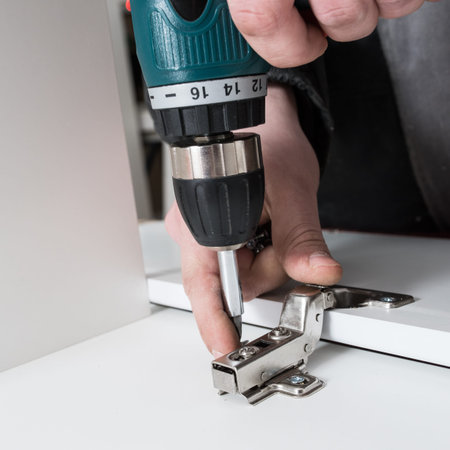 screwing the furniture hinge leaf to the white cabinet in the small wholesale furniture company