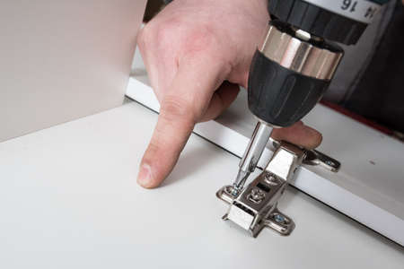 screwing the furniture hinge leaf to the white cabinet in the small wholesale furniture companyの写真素材