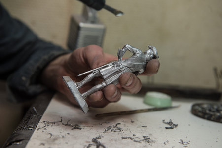 Saint-Petersburg, Russia - February 21, 2017: A small factory producing small batches pewter figurines. Master with a soldering iron removes blemishes after castingのeditorial素材