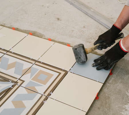 Specialist for laying tiles aligns the tiles with a carpenter's hammer in the living room of a city apartmentの写真素材