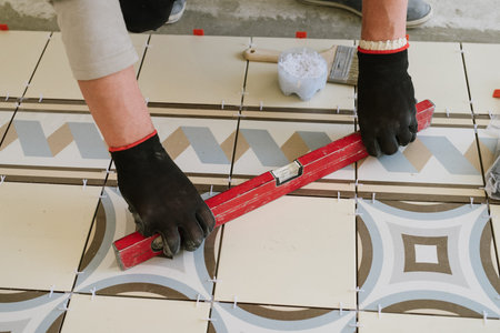The builder-mason controls the level of the horizontal tile with a tool in the living room of a...