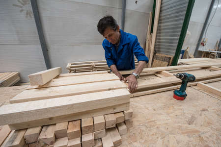 St. Petersburg, Russia - June 29, 2016: A middle-aged man carpenter in a timber warehouse makes from boards boards of boxes for storage and transportation of large-sized items.のeditorial素材