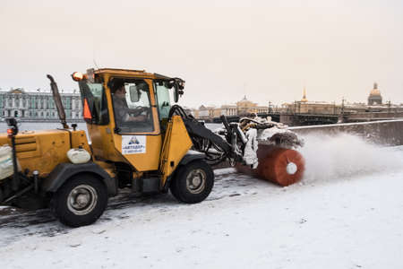 St. Petersburg, Russia - January 1, 2018: Snow removal from the pedestrian sidewalk by a rotating tractor brush in the historical center of the city on the Neva River embankment.のeditorial素材