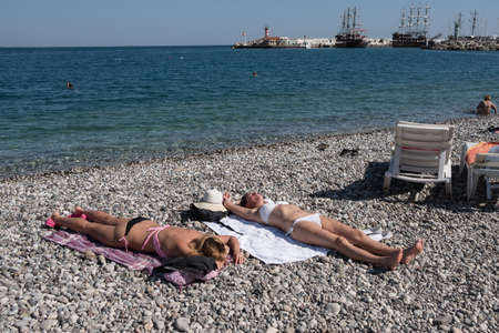 Kemer, Turkey - October 22, 2017: Tourists are resting on the beach of Kemer. two Girls lie on pebbles on towelsのeditorial素材