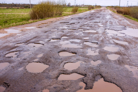 Road with lots of potholes, filled with rain. Bad condition of covering the highway, dangerous for...