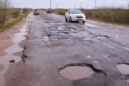 Novgorod Region, Russia-May 1, 2018: The road of local importance in emergency condition with a lot of potholes flooded with rain. Cars go with the risk of breakdownsのeditorial素材