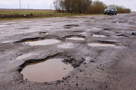 Novgorod Region, Russia-May 1, 2018: The road of local importance in emergency condition with a lot of potholes flooded with rain. Cars go with the risk of breakdowns